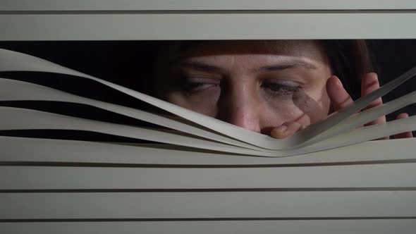 Woman looking out the window through the blinds to the street