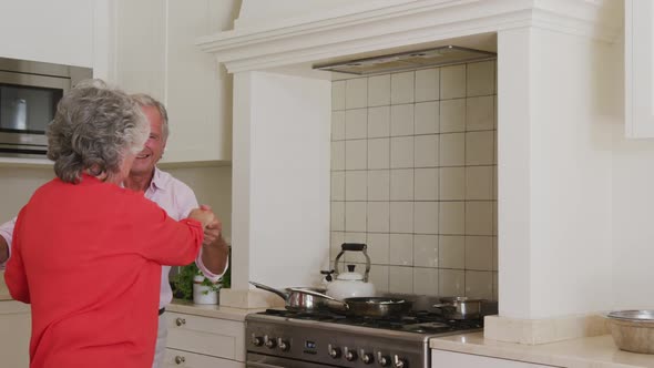 Happy caucasian senior couple having fun smiling and dancing in kitchen