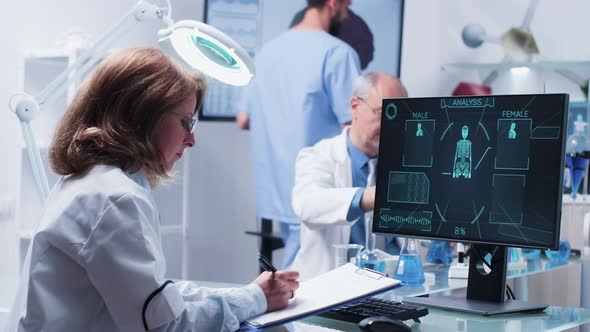 Woman Scientists Takes Notes on a Clipboard From a Computer Display