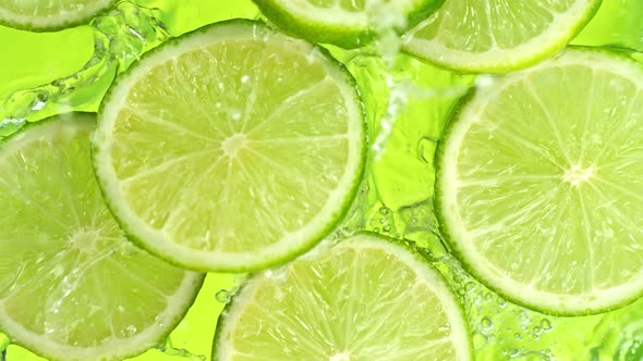 Super Slow Motion Shot of Lime Slices Falling Into Water on Green Background at 1000Fps