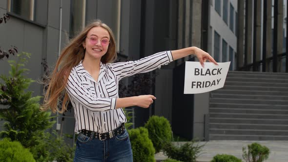 Happy Girl Holding Black Friday Inscription Text and Pointing on It. Shopping Mall Background