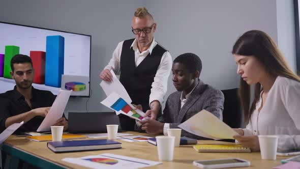 Portrait of Serious Boss Passing Paperwork to Employee Talking