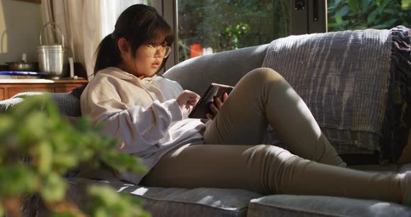 Asian girl lying on couch and using tablet
