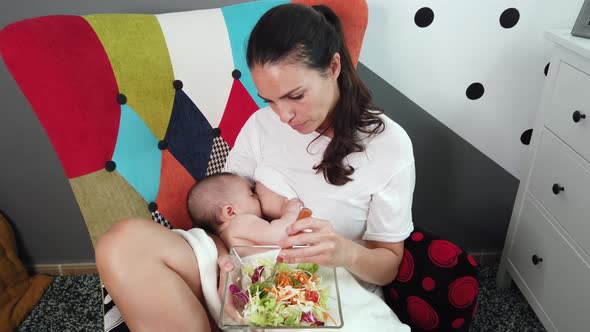 Woman breastfeeding baby with bowl of salad in hands