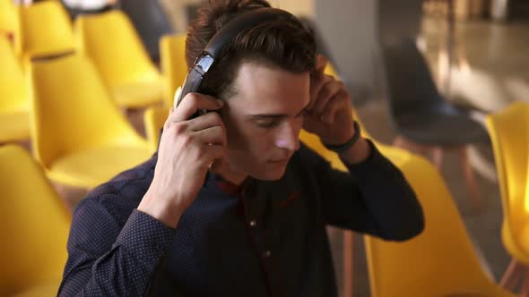 Attractive Young Guy Puts Headphones on His Head and Starts Working on His Laptop