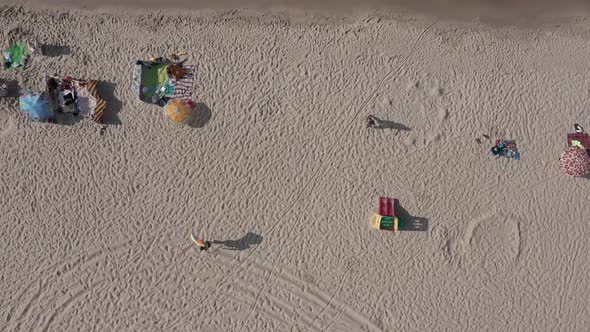 Aerial View Of People Relaxing, Sunbathing And Strolling At The Beach On A Sunny Day.