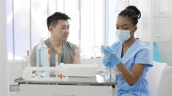 Crop View of Young Asian Man Watching How Medical Nurse in Protective Mask and Safety Gloves Filling