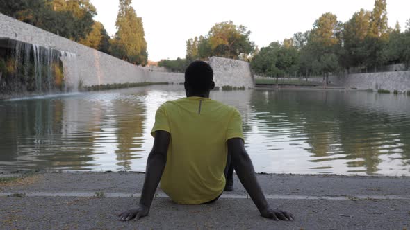 Black sportsman resting in park looking at water