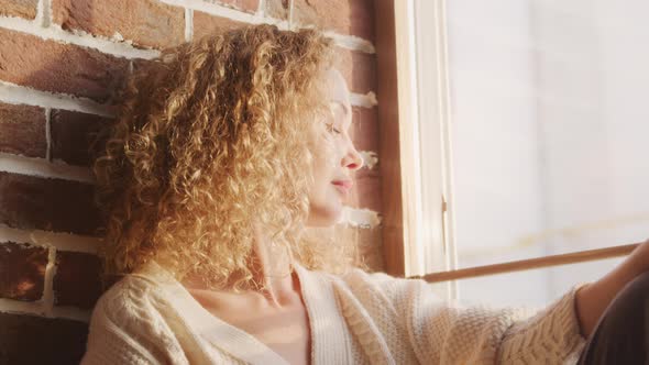 Curly Caucasian Woman Catching Sunlight on a Window Sill