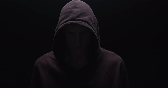 Silhouette of a man with a darkened face in a hood on a black background