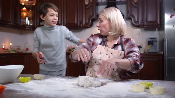 Caucasian Boy Bringing Phone To Woman Kneading Dough in Kitchen