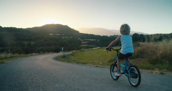 Happy Child Boy Ride Bicycle on Empty Countryside Road with Mountain View