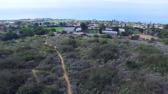 Aerial shot of a young man trail running on a scenic hiking trail.