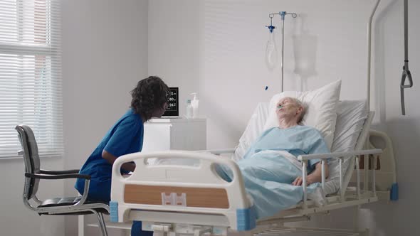 A Black Woman Cardiologist Doctor is Talking to an Old Man Patient Lying on a Hospital Bed