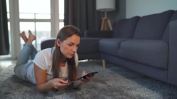 Woman Is Lying on the Floor and and Makes an Online Purchase Using a Credit Card and Smartphone