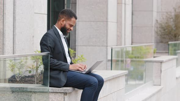 Serious Bearded Young Mixed Race Man Using Laptop Keeps on His Knees Notebook Sit Outdoors with