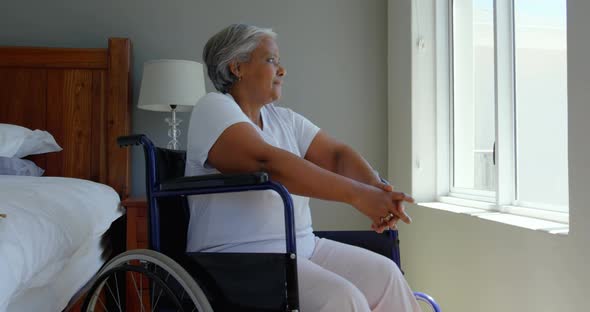 Side view of handicap senior black woman sitting on wheelchair near window  in bedroom at home 4k