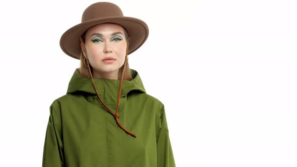 Woman in a Autumn Look in Studio in Green Parka and Hat Turns and Poses To the Camera