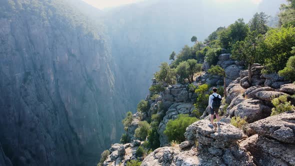 Traveler Guy with a Backpack Stands on a Cliff Overlooking Canyon