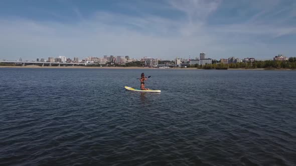 Caucasian Woman is Riding a SUP Board on the River in the City