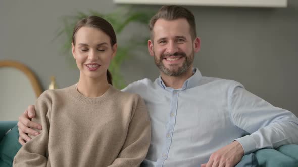 Portrait of Couple Smiling at Camera While Sitting on Sofa