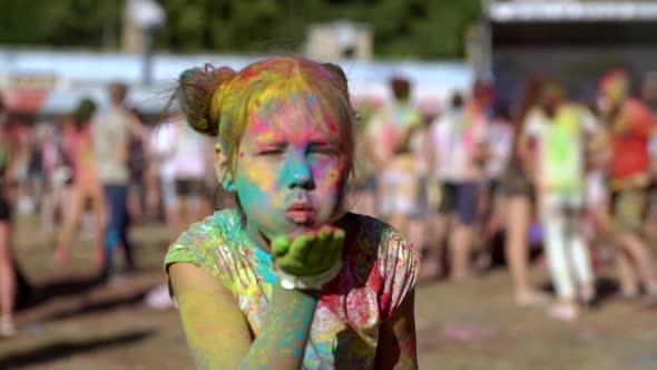 Little Girl Holding Holi Paints in Her Hands and Blowing Them Into the Camera