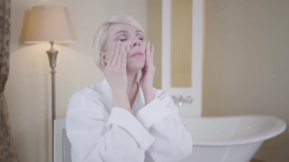 Blond Caucasian Woman Applying Face Cream. Portrait of Beautiful Adult Lady Taking Care of Face Skin