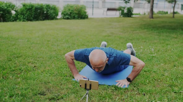 Powerful Old Male Athlete Makes Push Up While Looking on Smartphone Screen