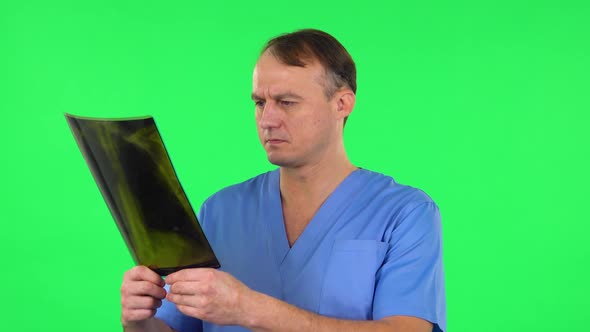 Male Doctor in Blue Coat Reviewing X-ray Pointing on Snapshot and Explains. Green Screen