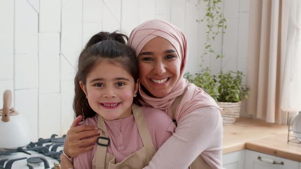 Muslim Mother In Hijab Embracing Daughter Smiling To Camera Indoor