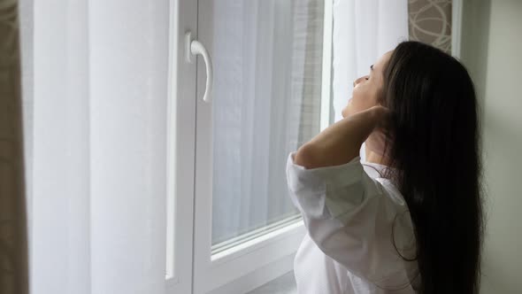 Young woman in the morning opens the curtains at the window