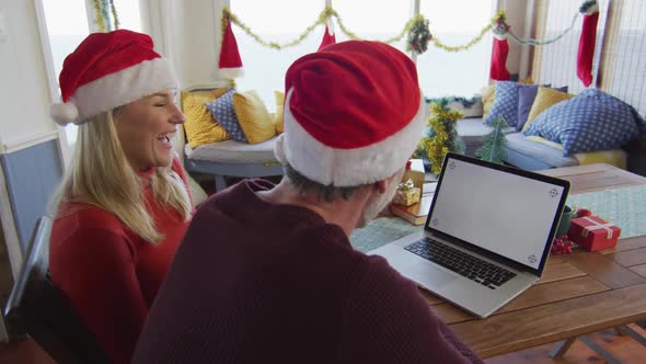 Happy caucasian mature couple wearing santa hats using laptop with copy space