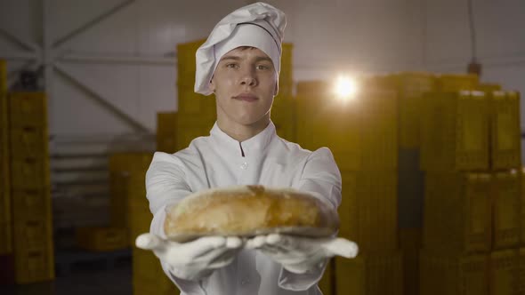 The Baker in Uniform Presents at Camera a Freshly Baked Loaf of Bread in Bakery