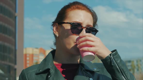 Young Woman Drinking Coffee on the Street, Typing Texting a Mobile Phone, While Walking in an Urban