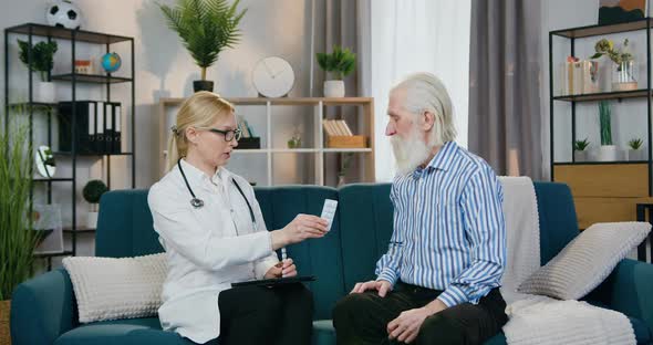 Doctor Giving Tablets to Her Old Male Patient and Telling How to Take them During Home Visit