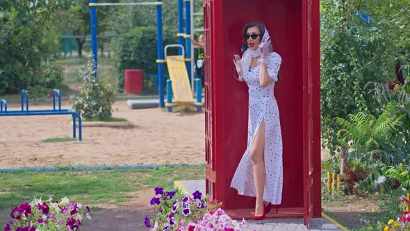 Beautiful Young Woman Happily Speaks on the Phone in an English Style Red Telephone Booth