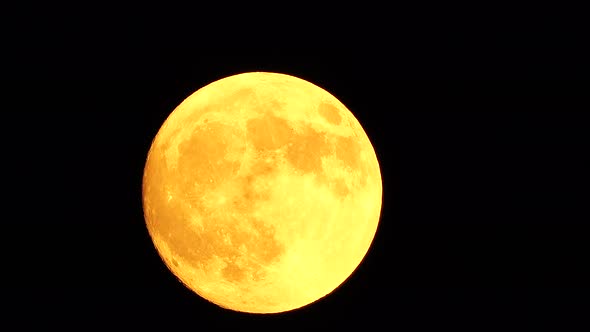 Glowing Yellow Huge Full Moon As Seen From Earth Through the Clouds Against Starry Night Sky