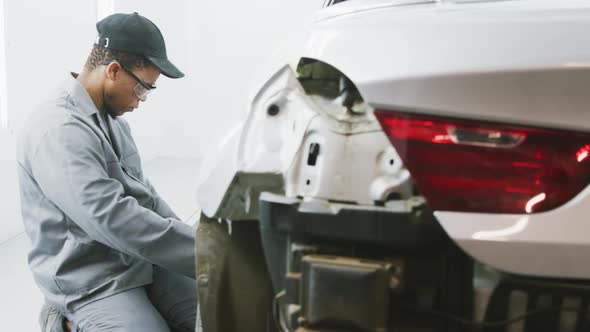 African American male car mechanic kneeling by a car and repairing it
