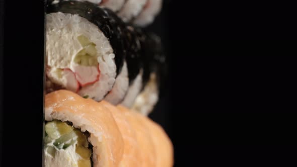 Vertical Video. Sushi Rolls Rotates in a Plastic Container on a Black Background