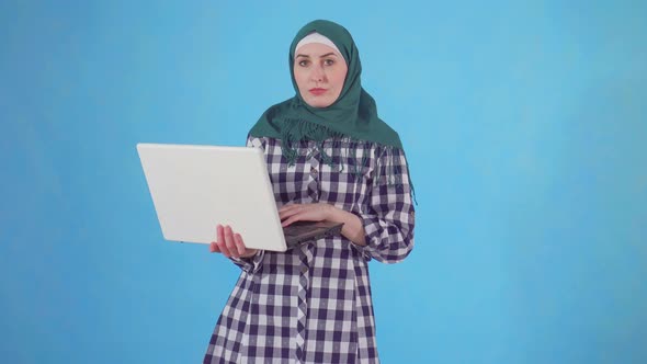 Young Muslim Woman Uses Laptop on Blue Background