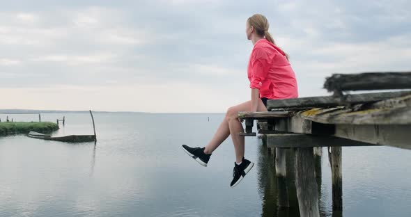 Woman sitting with her legs dangling on old wooden pier.