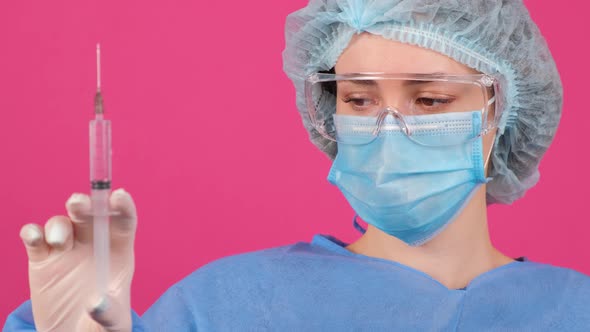 Professional Female Doctor Holds a Syringe with a Vaccine on a Pink Background