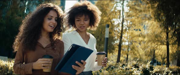 Video of smiling businesswomen discussing with digital tablet outdoors.