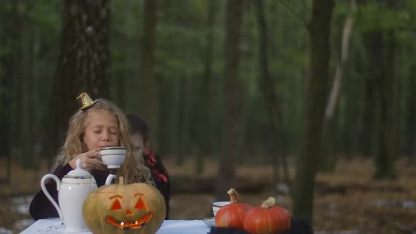 Beautiful Girl Sitting at Table in Forest Drinking Tea As Vampire Scaring Kid