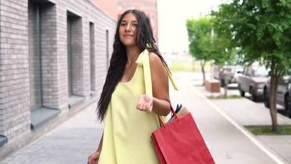 A Beautiful Girl in a Yellow Dress is Walking Down the Street After Shopping