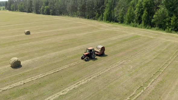 Aerial: Farmer on a Tractor Baling and Wrapping Hay Rolls in a Meadow in Hot Sunny Weather