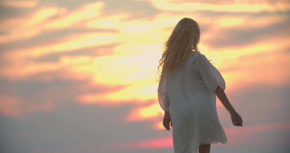 Young Blonde Woman in White Dress is Dancing While Looking at the Sunset