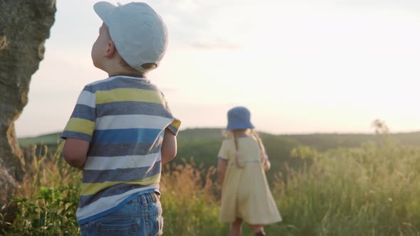 Cute Preschool Little Baby Girl and Boy Sitting on Top of Mountain in Tall Grass Before Sunset