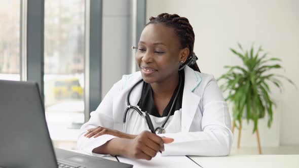 Young African American Woman Doctor with Headset Having Chat or Consultation on Laptop