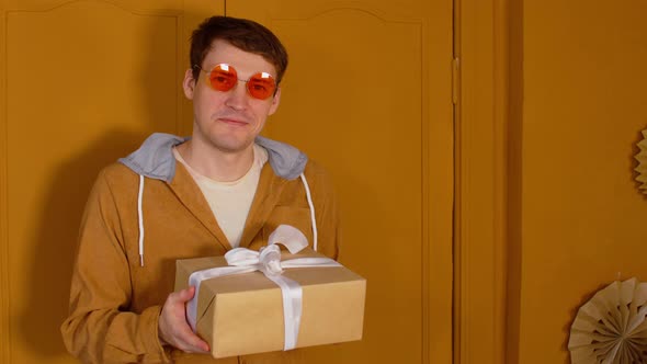 Young man in bright glasses with wrapped gift box.